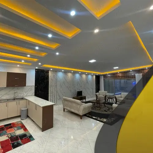 کابینت های آشپزخانه و مبلمان سفید و سقف نورپردازی شده با نور زرد سالن نشیمن ویلا در محمودآباد