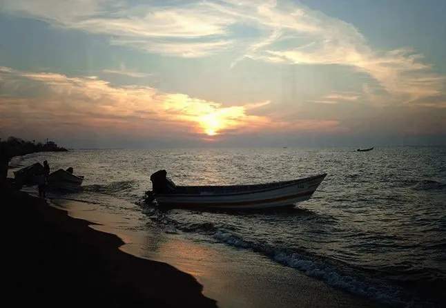غروب آفتاب در کنار دریای مواج و قایق به ساحل نشسته 5556458