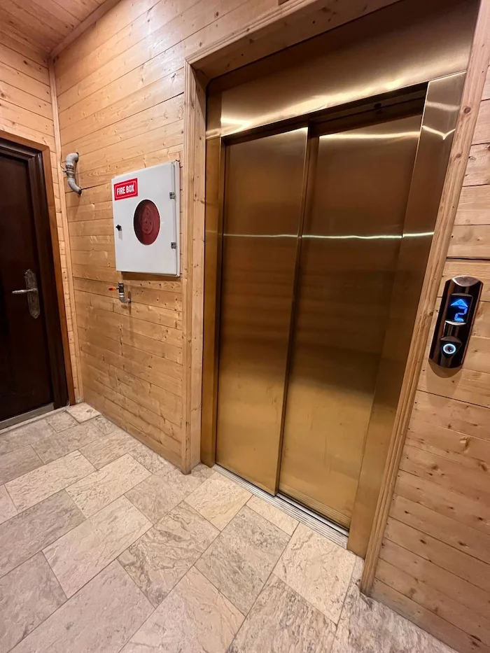 آسانسور فلزی طلایی در راه پله با دیوارهای چوبی برج روشا 45845684